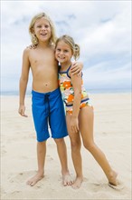 Brother (8-9) and sister (6-7) embracing on beach