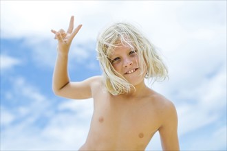 Boy (8-9) showing peace sign against blue sky