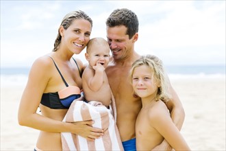 Family with two children (12-17 months, 8-9) embracing on beach