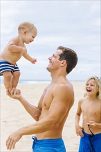 Father playing with sons (12-17 months, 8-9) on beach