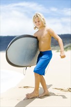 Boy (8-9) standing on beach and holding surfboard