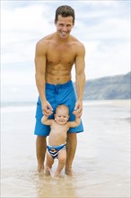 Son (12-17 months) learning to walk with father on beach