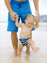 Son (12-17 months) learning to walk with father on beach