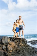 Man and children (6-7, 8-9) standing on rock by sea