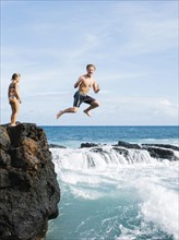Girl (6-7) standing on cliff and man jumping into sea