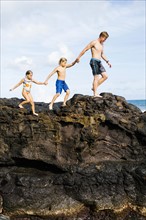 Young man walking on rock with kids (6-7, 8-9)