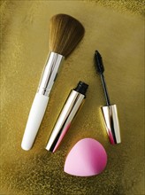 Mascara, make-up brush and small sponge on shiny background