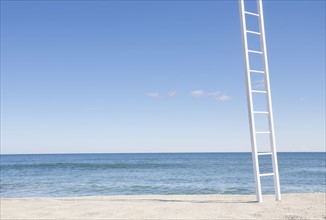 White ladder on empty beach with blue ocean in background