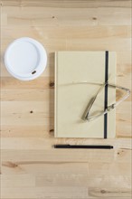 Disposable cup, diary, eyeglasses and pen on wooden desk