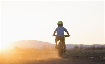 USA, Colorado, Rear view of boy (8-9) cycling at sunset
