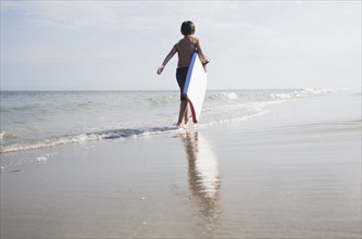 Boy (8-9) walking and carrying body board in empty beach