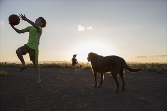 USA, Colorado, Boy (8-9) playing ball next to chocolate Labrador and little girl (4-5) running in background