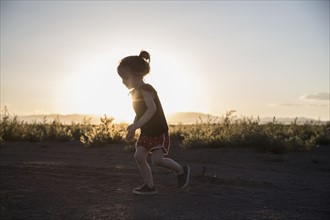 USA, Colorado, Little girl (4-5) running on dirt road at sunset