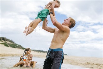 USA, Hawaii, Kauai, Young man with three younger siblings (12-17 months, 4-5, 6-7) playing at beach