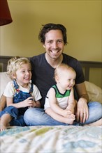Father with sons (12-17 months, 4-5) sitting on bed