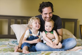 Father with sons (12-17 months, 4-5) sitting on bed
