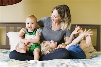 Mother with sons (12-17 months, 4-5) sitting on bed