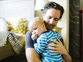 Father embracing baby boy (12-17 months) in bedroom
