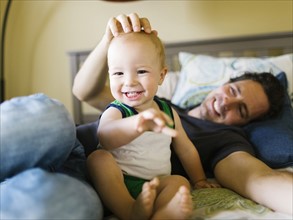 Father stroking baby boy (12-17 months) in bedroom