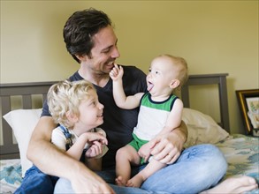 Father playing with sons (12-17 months, 4-5) in bedroom
