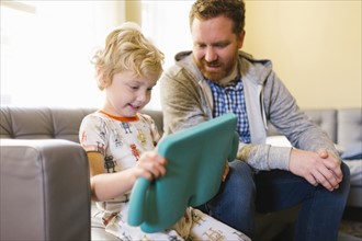 Boy (4-5) and man using digital tablet on sofa in living room