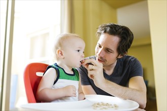 Father feeding son (12-17 months) with breakfast cereals