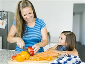 Mother cutting vegetables with daughter (6-7) in kitchen