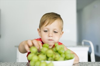Boy (2-3) eating white grapes in kitchen