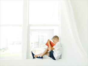 Boy (6-7) reading book by window