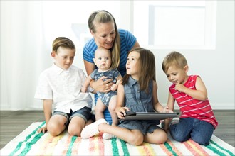 Mother with children (6-11 months, 2-3, 6-7) using digital tablet at home