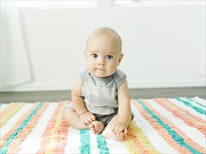Portrait of baby boy (6-11 months) sitting on colorful carpet