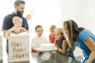 Parents with children (6-11 months, 2-3, 6-7) looking at daughter (6-7) blowing birthday candles