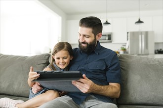 Father with daughter (6-7) using digital tablet in living room