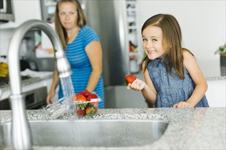 Mother looking at daughter (6-7) holding strawberry in kitchen