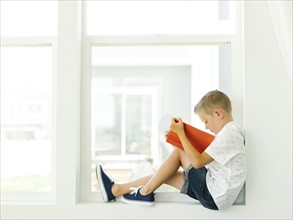Boy (6-7) reading book by window