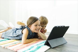 Siblings (2-3, 6-7) lying down on carpet and watching digital tablet