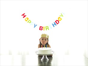Girl (6-7) in paper crown blowing candles on birthday cake