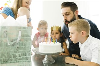 Family with four children (6-11 months, 2-3, 6-7) blowing candles on birthday cake