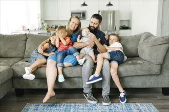 Family with four children (6-11 months, 2-3, 6-7) spending time on sofa