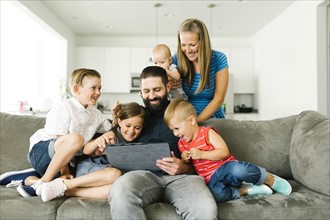 Family with four children (6-11 months, 2-3, 6-7) using digital tablet