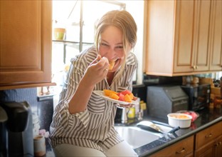 Woman in kitchen eating fruit salad