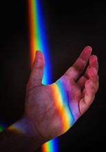 Man's hand with rainbow light against black