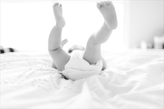 Baby girl (6-11 Months) lying down on bed with feet in air