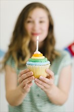 Mid adult woman holding cupcake with birthday candle