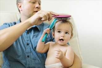 Father and baby girl (12-17 months) brushing hair after bath