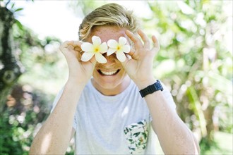 Portrait of young man holding gardenia flowers in front of eyes