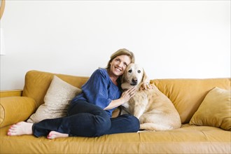 Portrait of woman embracing Labrador Retriever on sofa