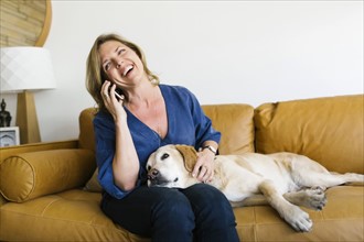 Woman stroking Labrador Retriever and using mobile phone