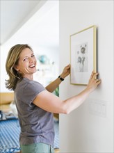 Smiling woman hanging picture frame on wall