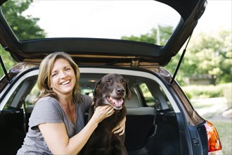 Portrait of woman stroking Labrador Retriever in car trunk